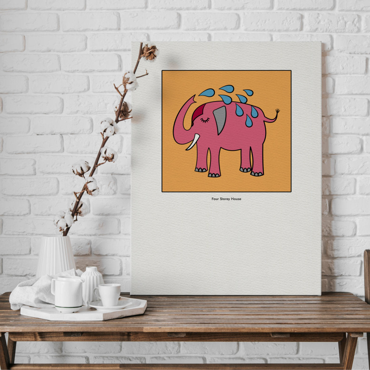 Original A2 Art Print - Pink Elephant featuring a whimsical pink elephant with water droplets on an orange background, displayed on a wooden table against a white brick wall.