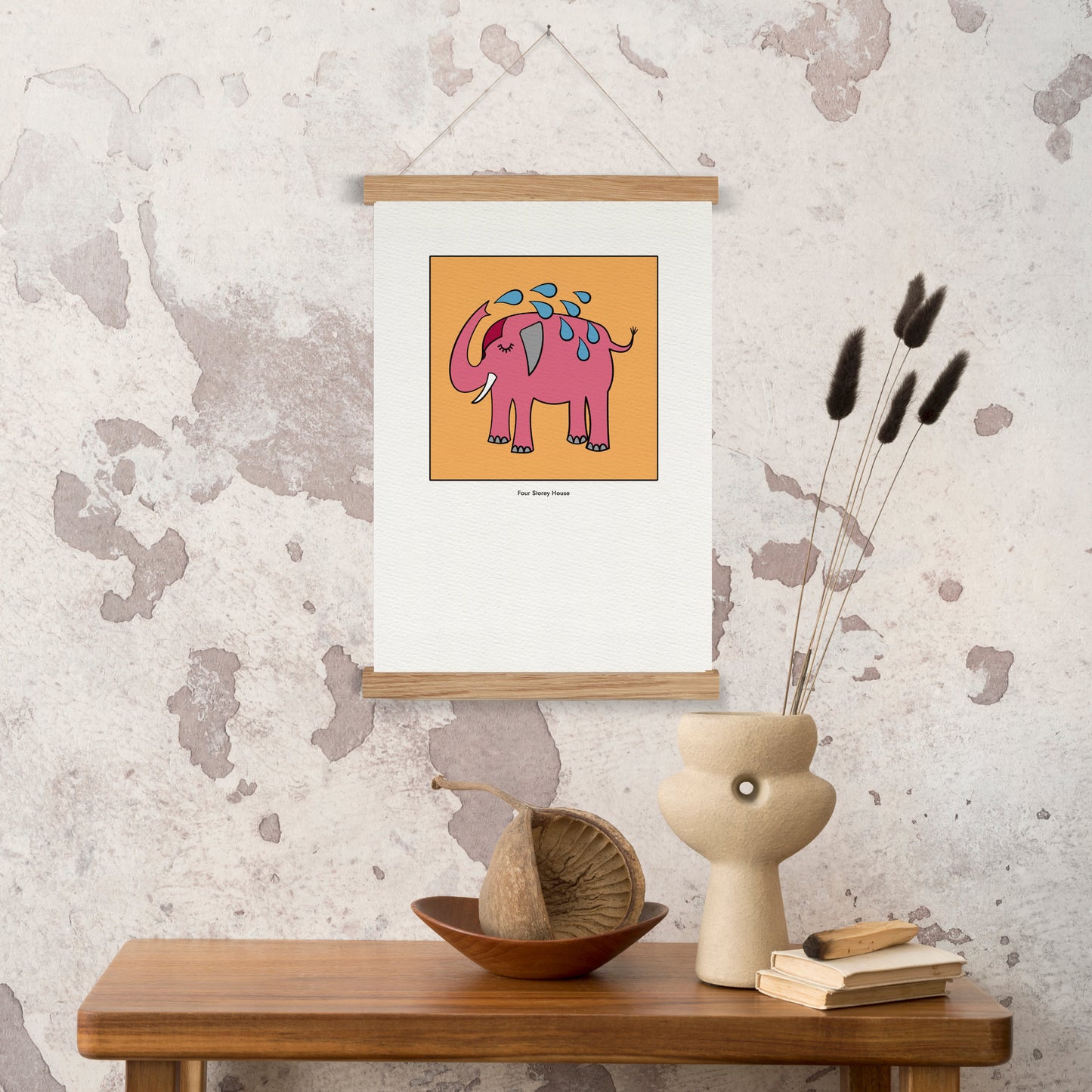 Original A2 Art Print - Pink Elephant hanging on textured wall above wooden table with decorative vase, dried flowers, and books in a cozy, minimalist interior.