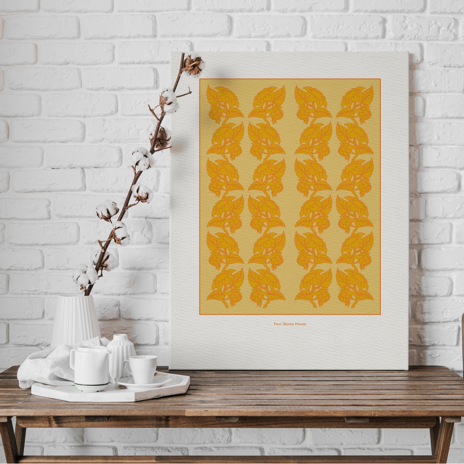 Original A2 Art Print - Sunflowers in Yellow & Orange displayed on a wooden table against a white brick wall, featuring a bold pattern of stylized yellow and orange sunflowers.